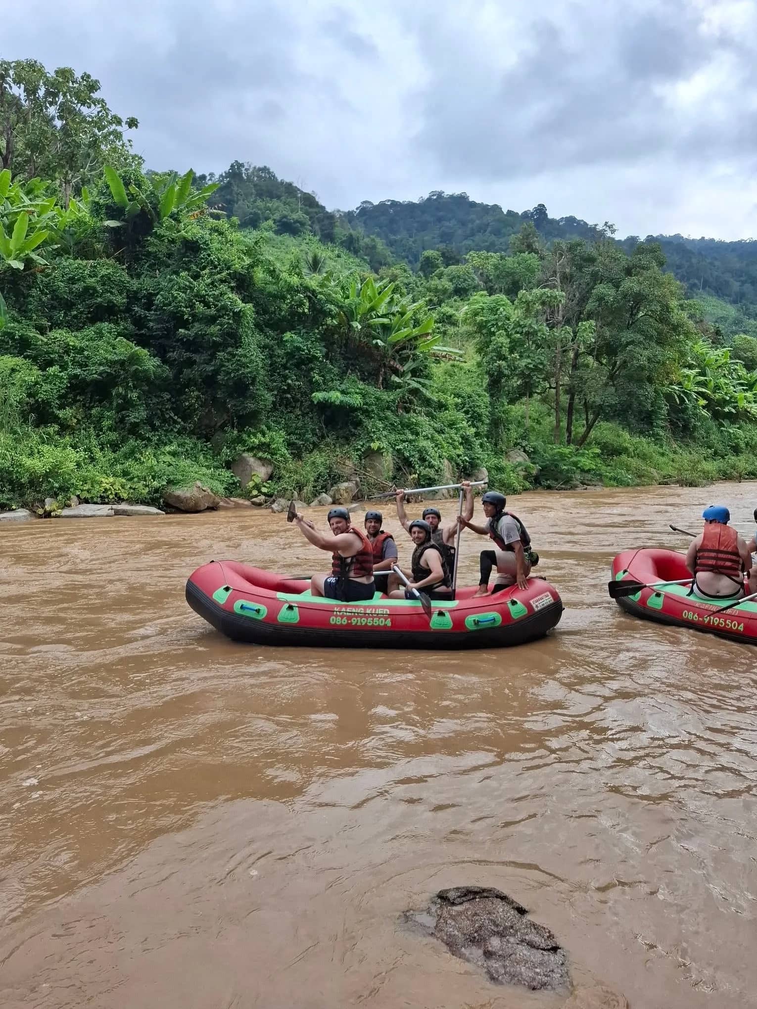 Rafters raise their paddles in red rafts on a brown river lined with green jungle
