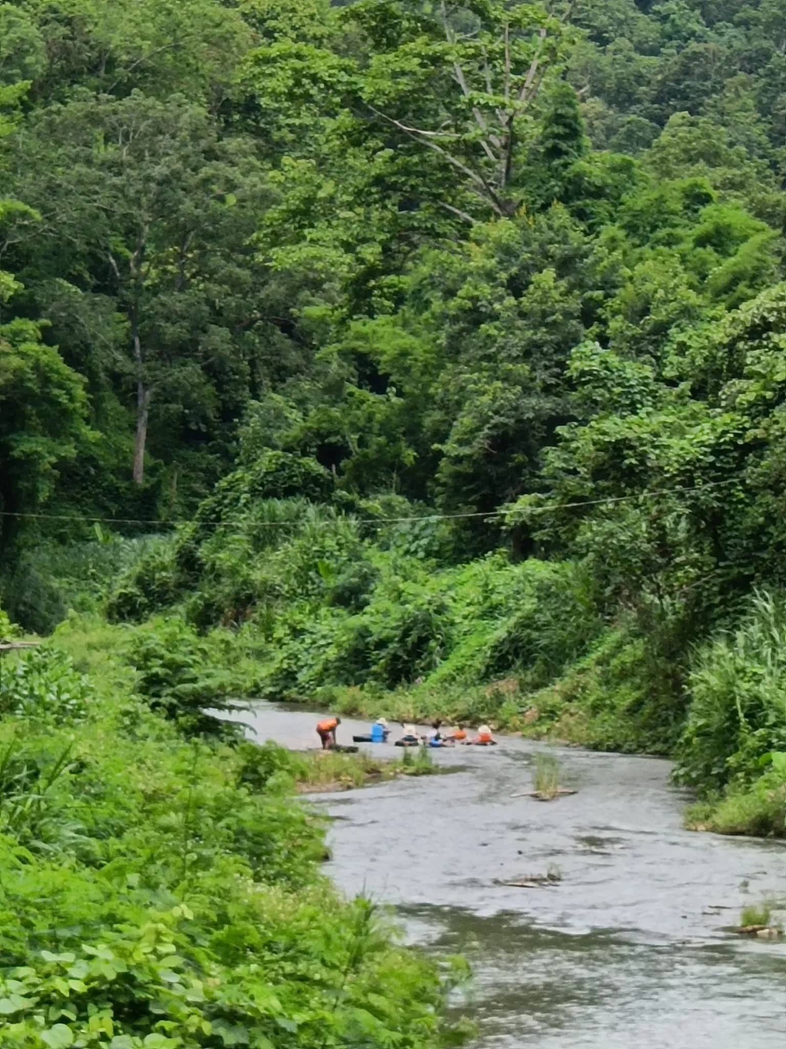 A shallow river winds through a steep green jungle valley with tubers far downstream