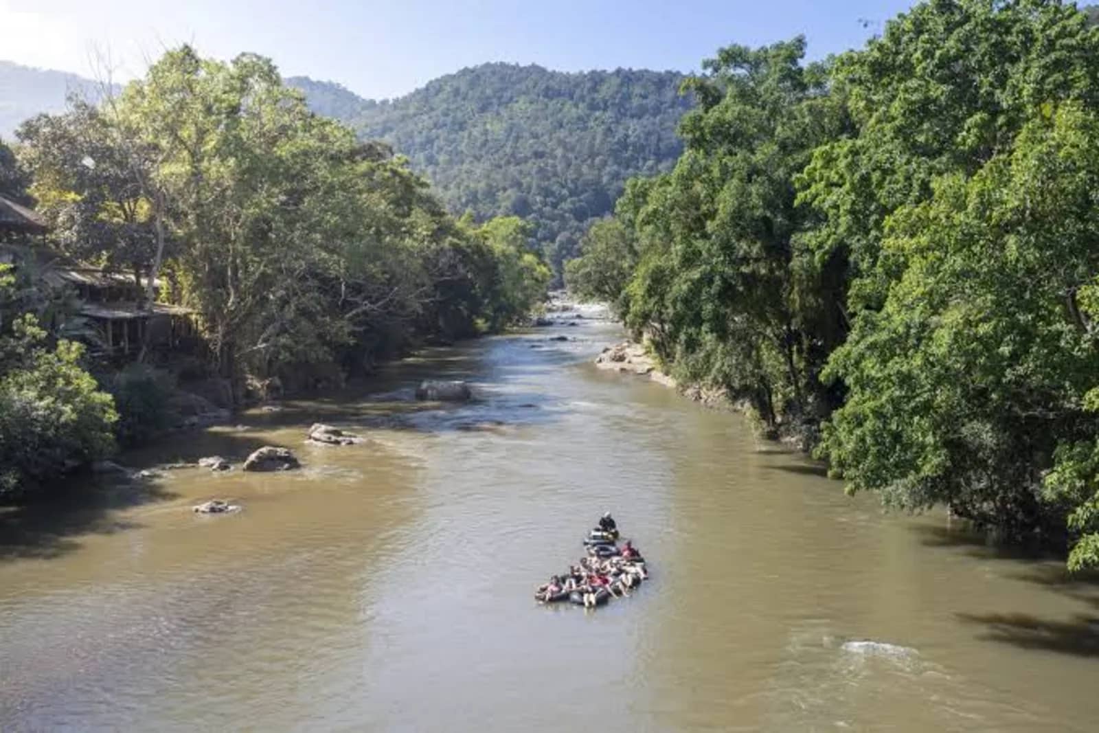 A group of tubers linked together drifts down a wide river between forested banks