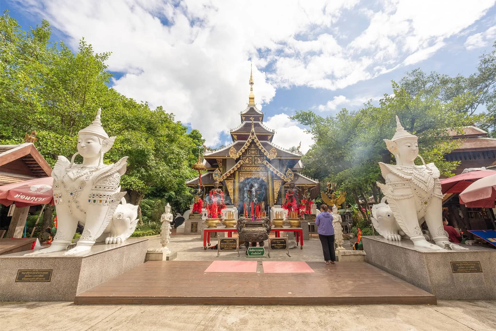 Two white mythical guardian statues flank the path to an ornate temple shrine