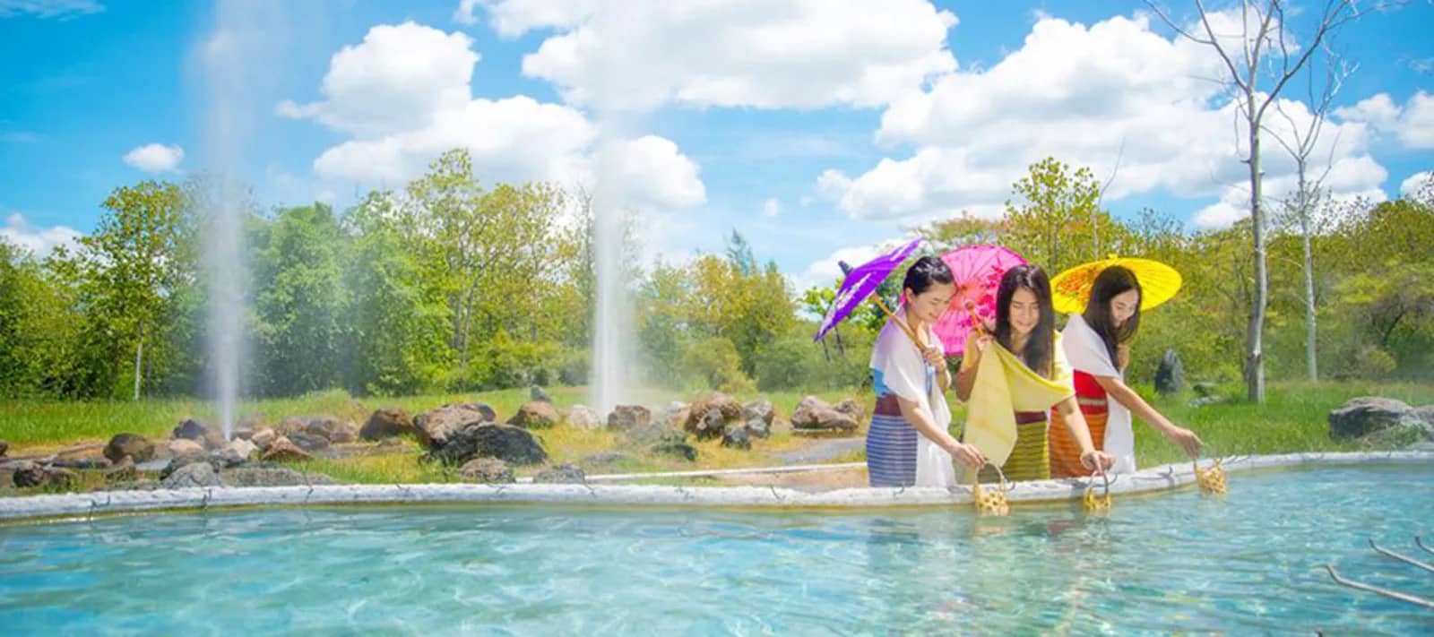 Women with paper parasols dip egg baskets into a hot spring pool as geysers spray behind them