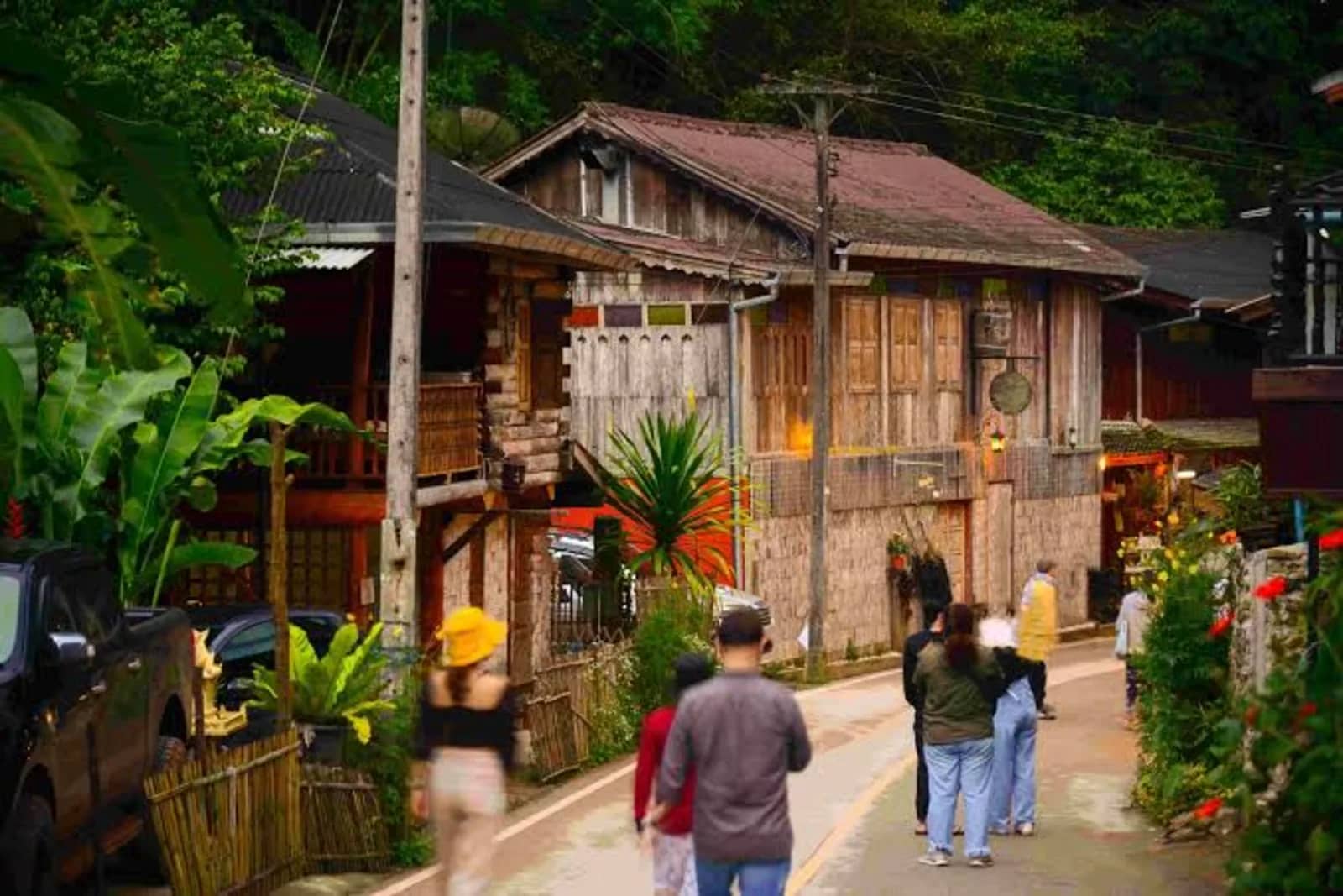 Visitors walk along a narrow lane past old wooden houses in Mae Kampong village