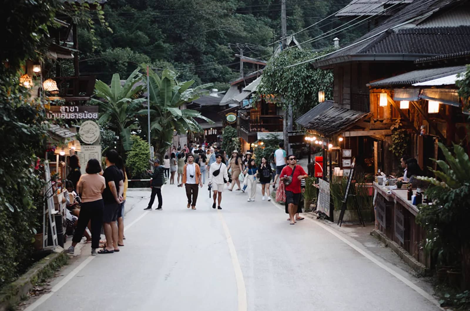 Visitors walk along the main road of Mae Kampong past lit wooden shops and cafes