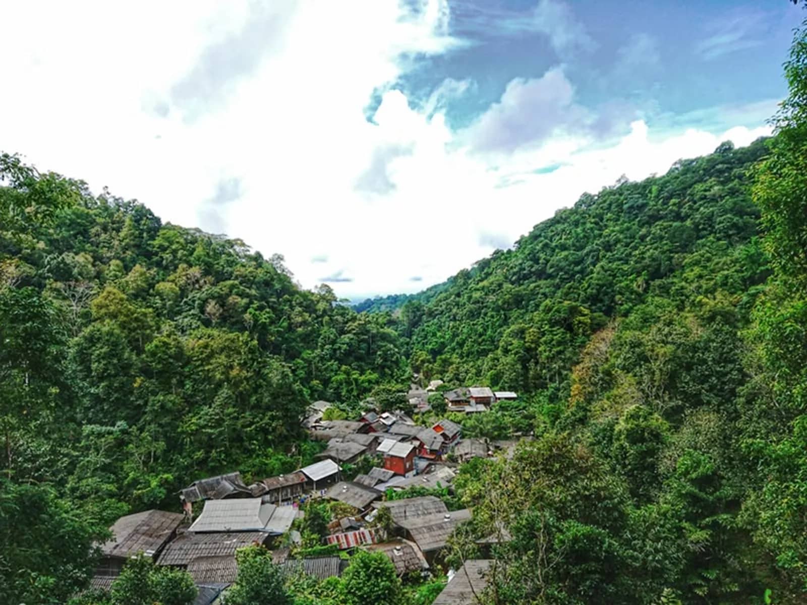 The roofs of Mae Kampong village sit in a deep forested valley under a cloudy sky