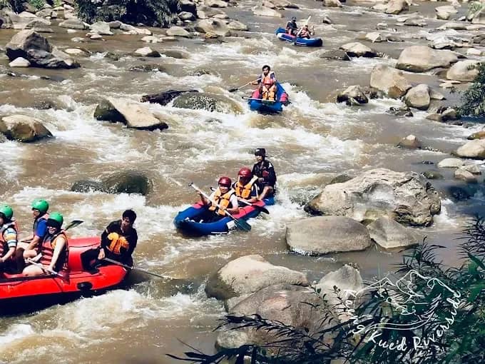 A red raft and small inflatable kayaks navigate rapids between large boulders