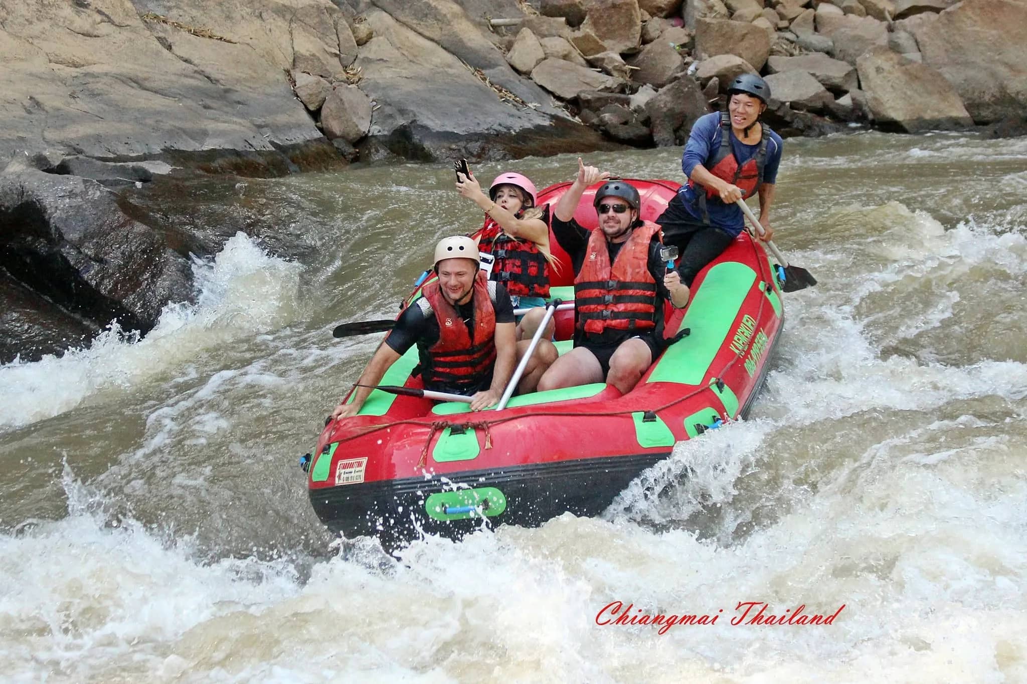 Rafters wave and cheer as their red raft rides a rapid between rocks