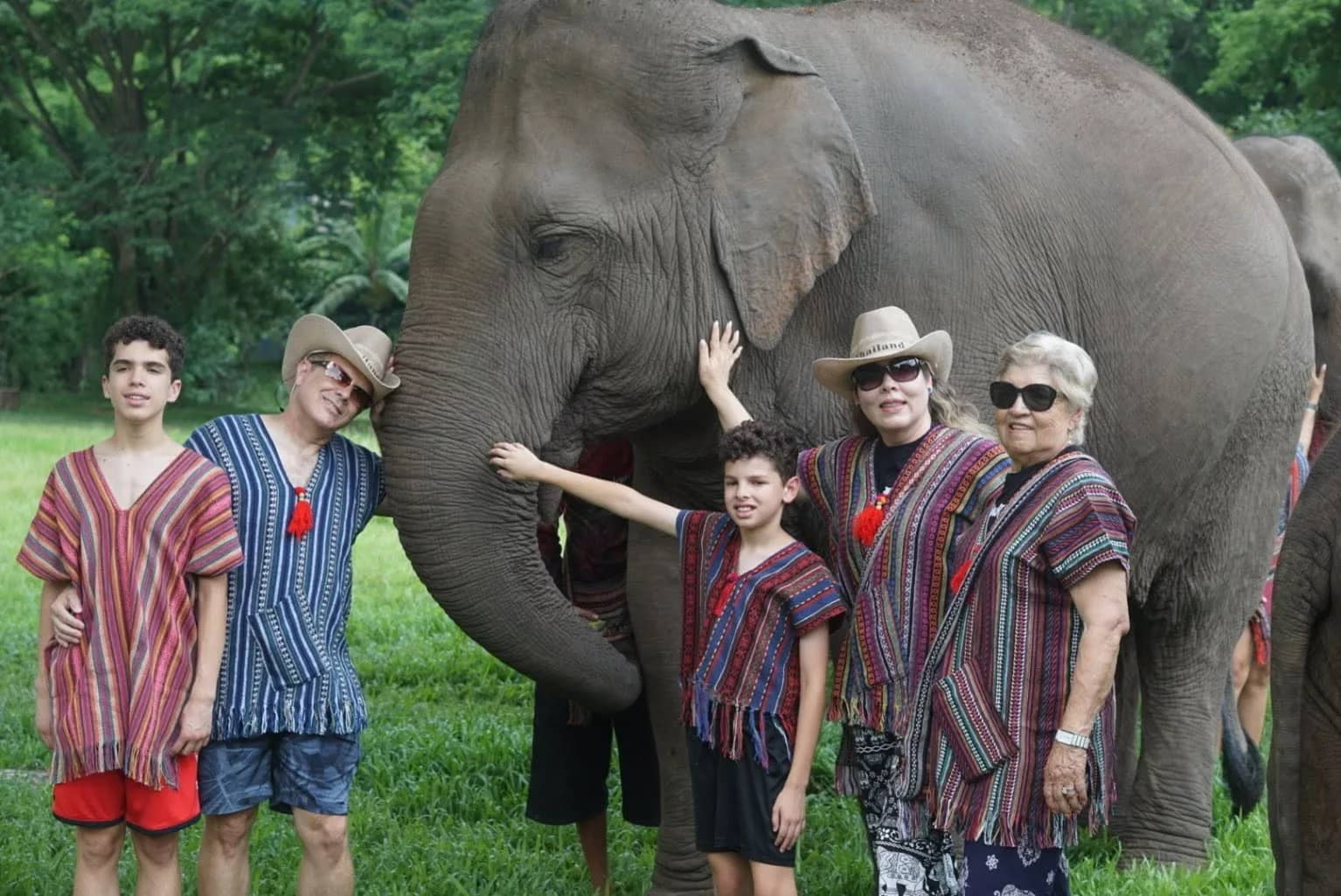 A family in striped woven tops poses beside an elephant as a boy reaches out to touch it.