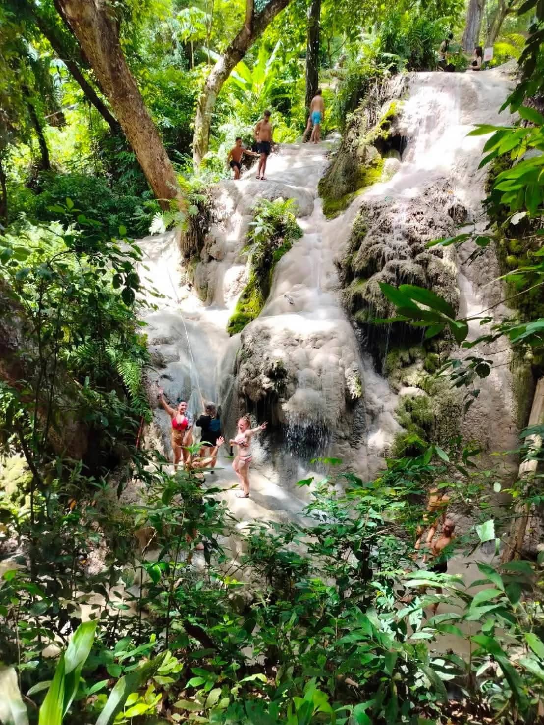 Visitors climb up a white limestone waterfall surrounded by lush jungle.