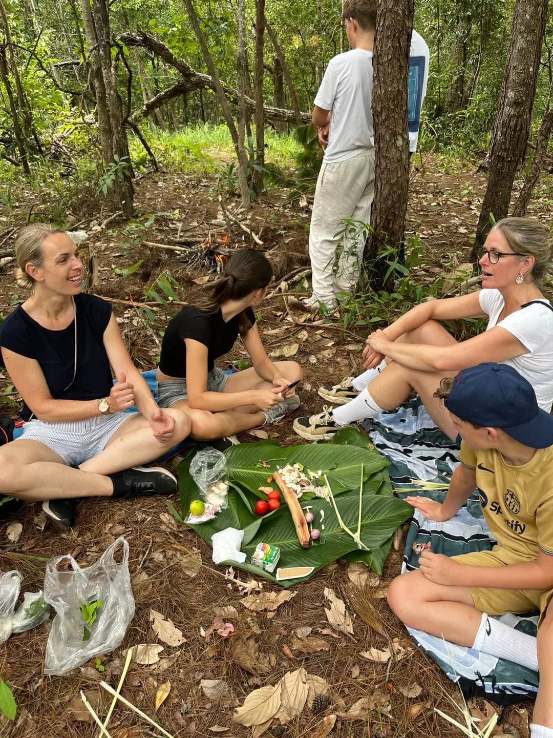 Trekkers sit on the forest floor sharing a meal laid out on banana leaves.
