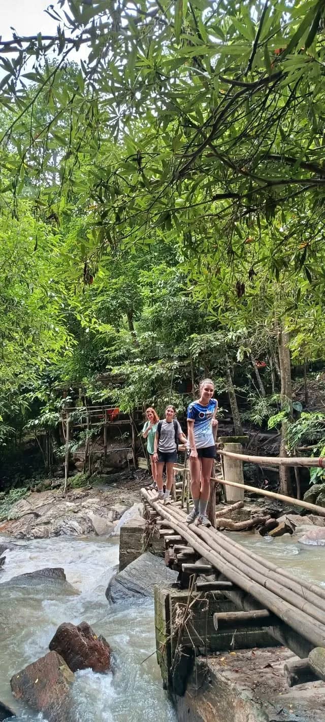Visitors walk along a wooden boardwalk next to a rushing rocky stream on the way to a waterfall.