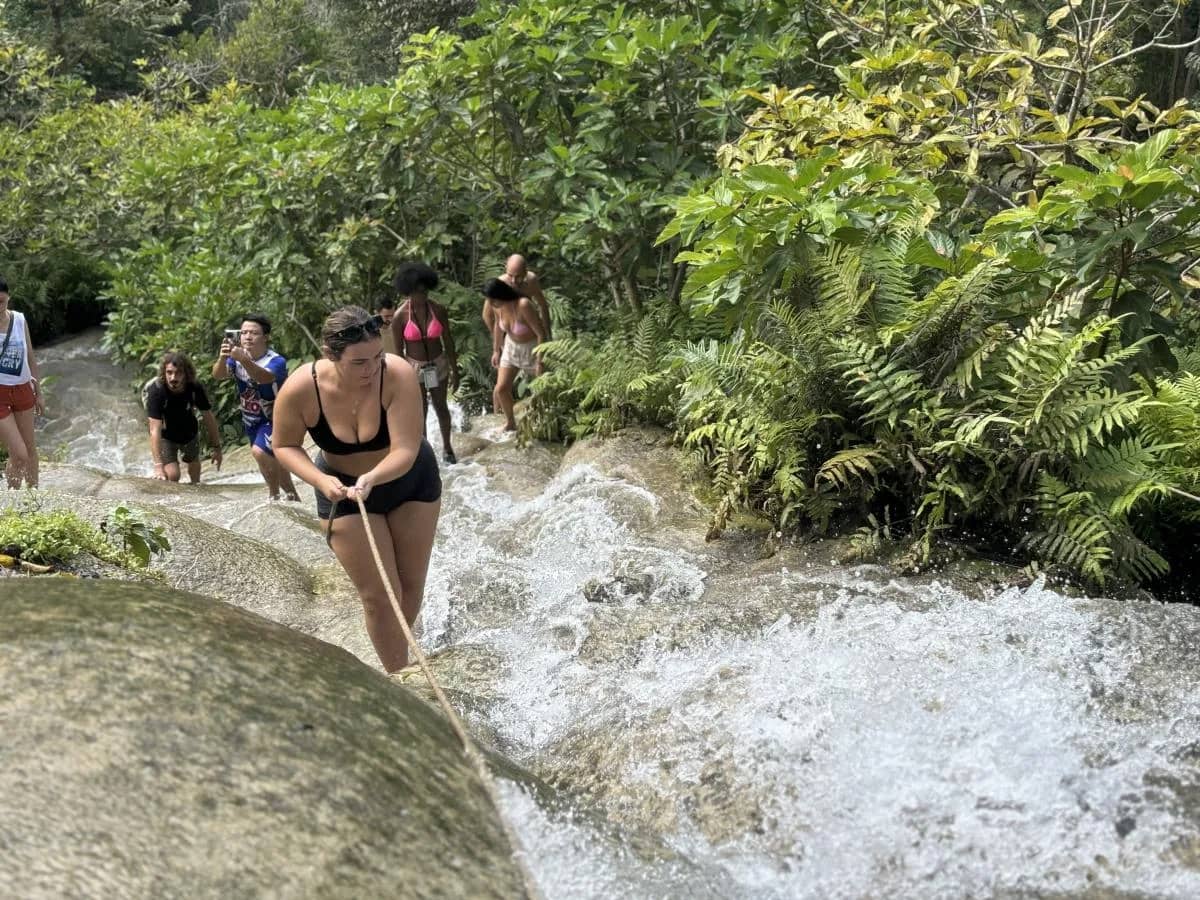 Visitors climb up the rushing Sticky Waterfall using a rope tied along the rocks