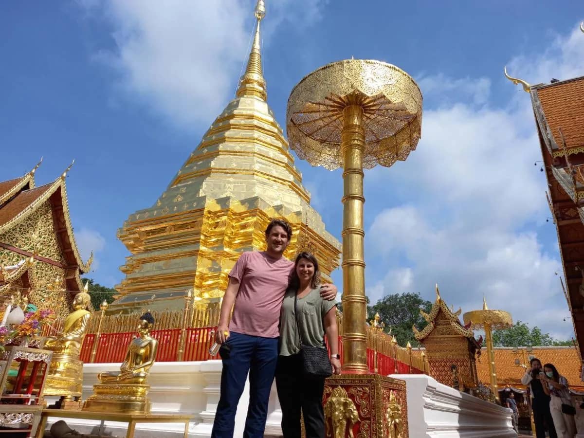 A couple poses in front of the golden chedi and parasol at Wat Phra That Doi Suthep
