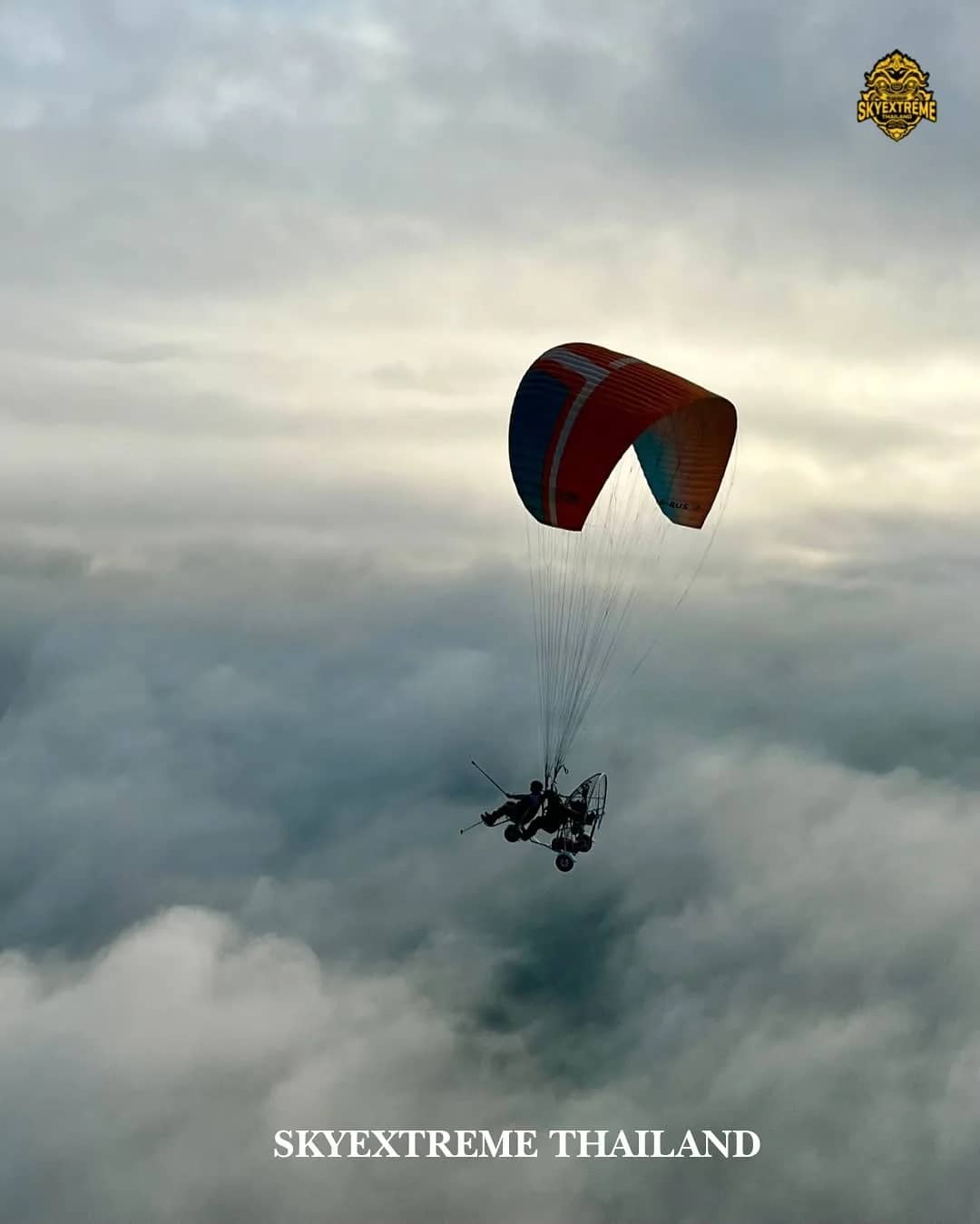 A paramotor with a red and blue wing flies above a thick sea of clouds near Chiang Mai
