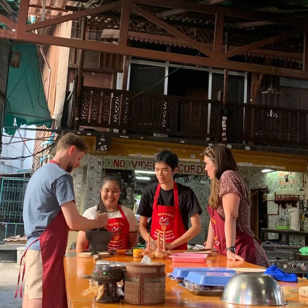 Guests in red aprons prepare ingredients at a counter with their instructor at the cookery centre