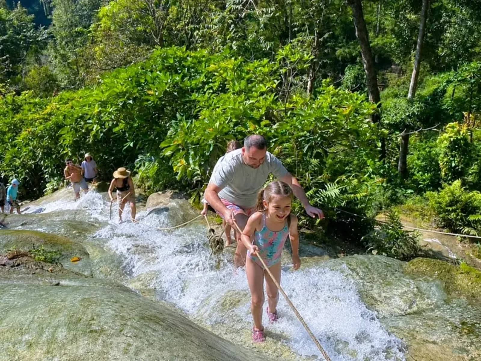 A man and a young girl climb the limestone steps of the Bua Tong Sticky Waterfall with a rope