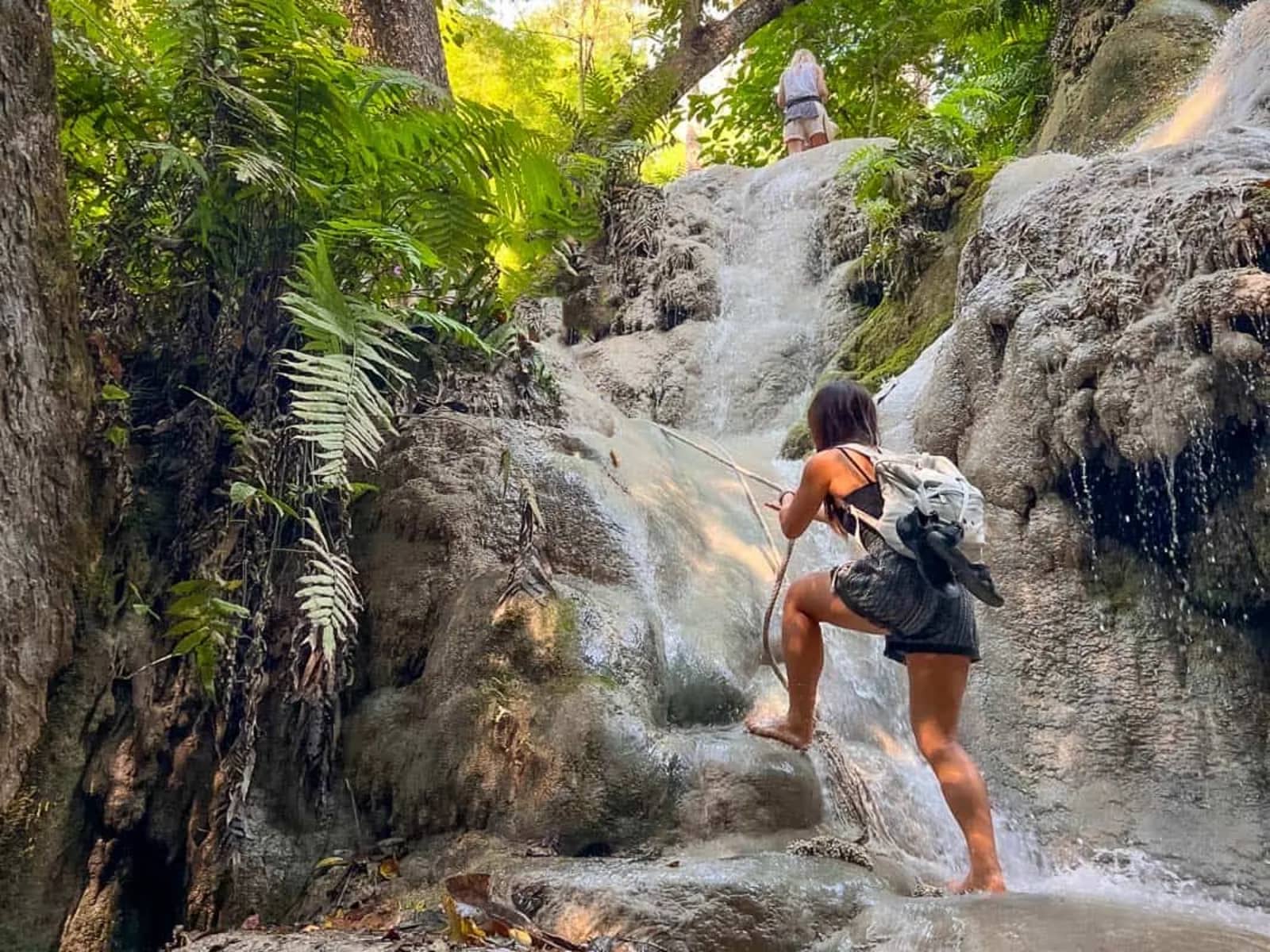 A hiker grips a rope while climbing the textured limestone rocks of the sticky waterfall.