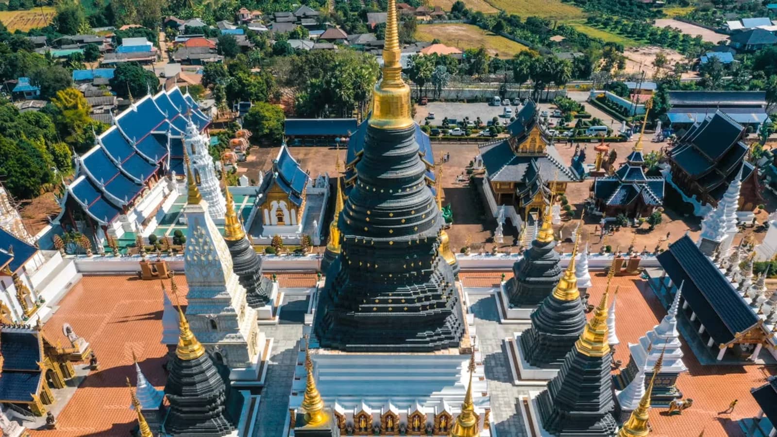 Aerial view of the dark chedi and blue-roofed halls of Wat Ban Den temple in Chiang Mai province