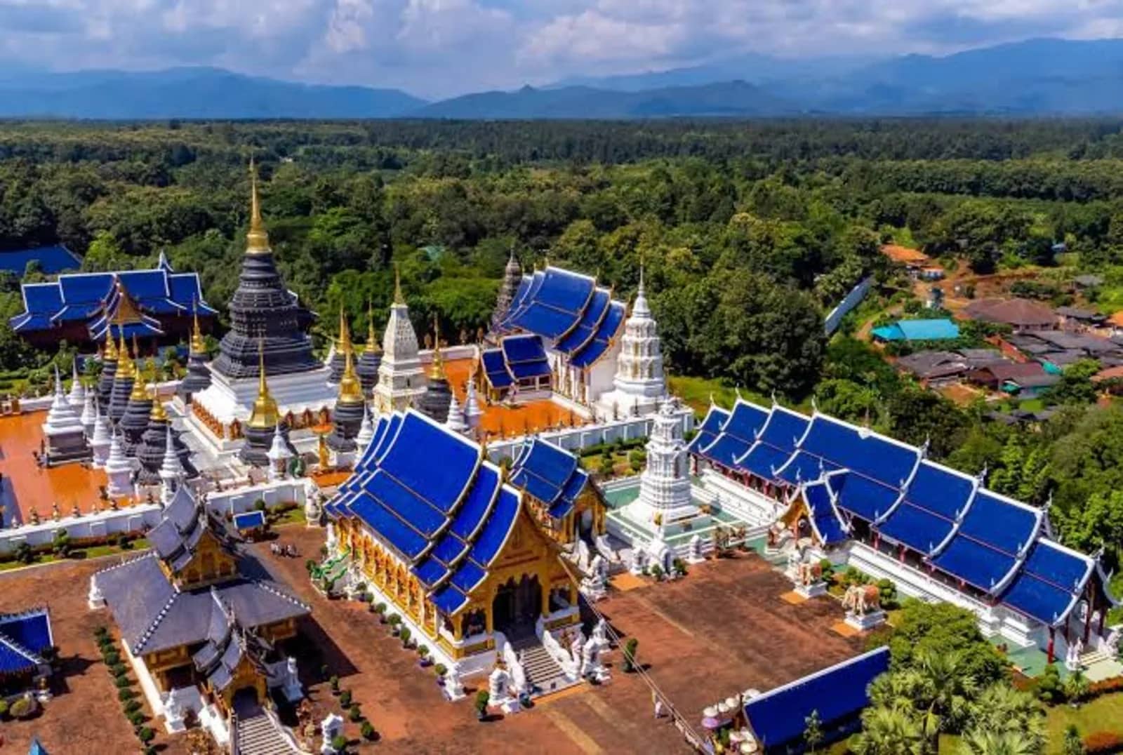 Aerial view of Wat Ban Den with blue tiled roofs, white chedis and forest stretching to the mountains
