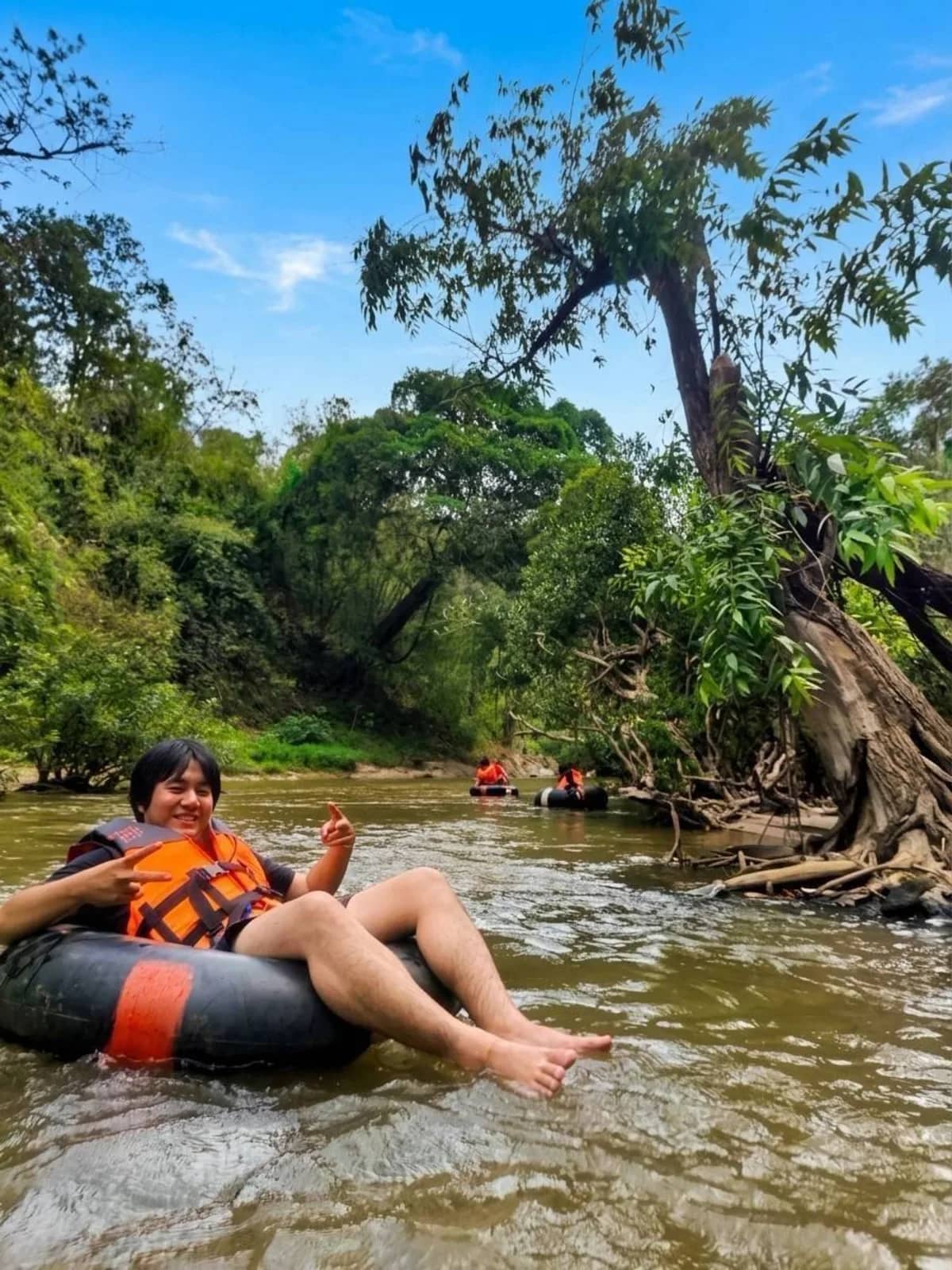 A rider in a life jacket relaxes on an inner tube floating down a shallow jungle river
