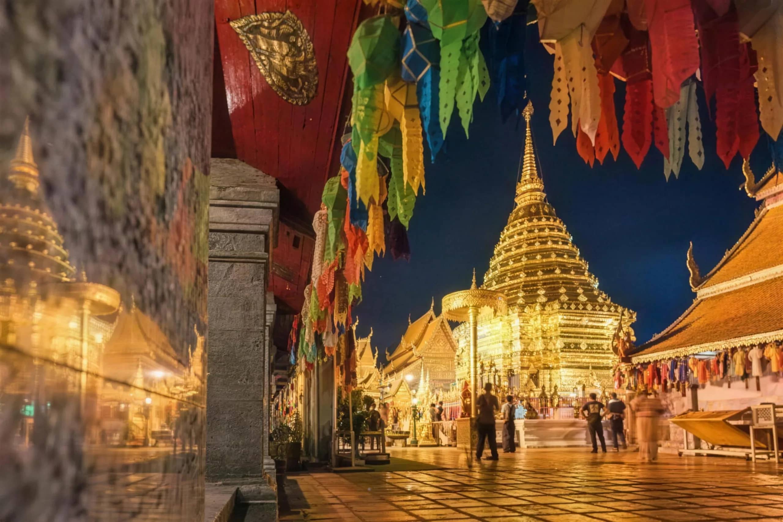 The golden chedi of Wat Phra That Doi Suthep glows at night framed by hanging paper flags
