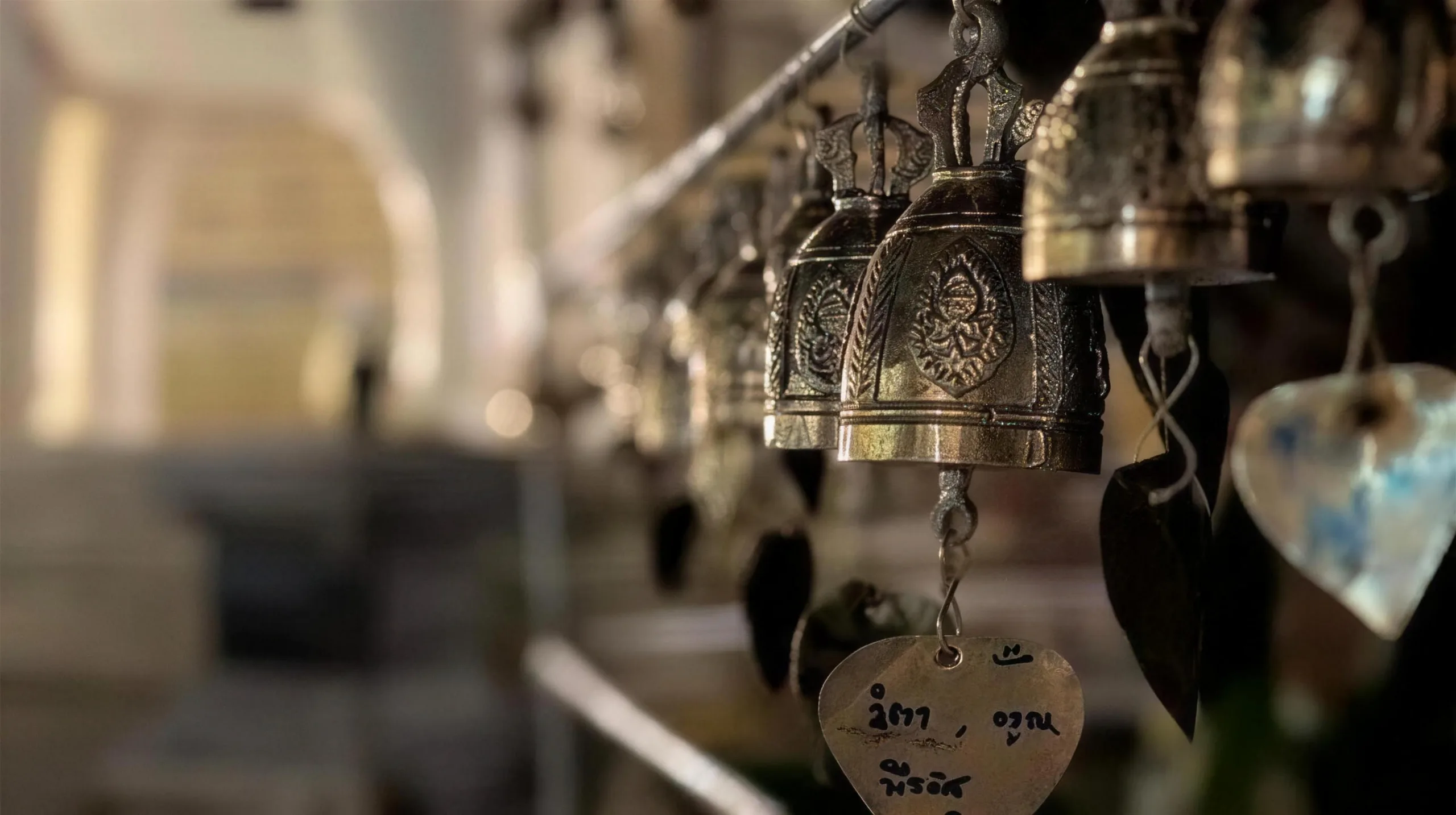 A row of small brass temple bells with heart-shaped wish tags hangs along a railing