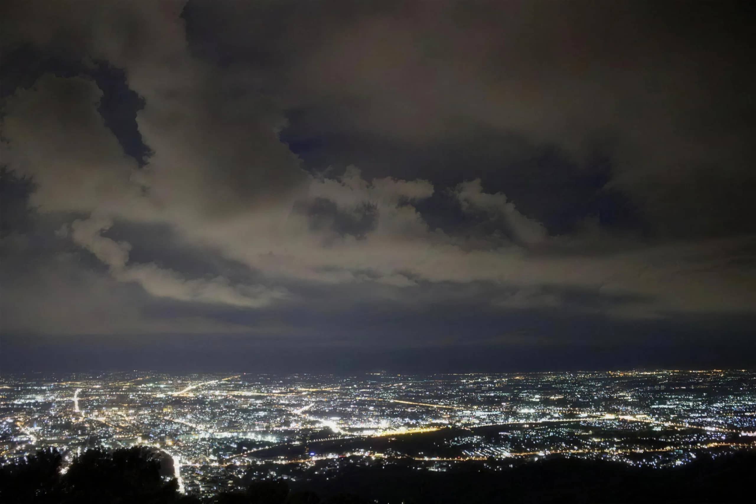 The lights of Chiang Mai city spread out under a cloudy evening sky seen from the mountain