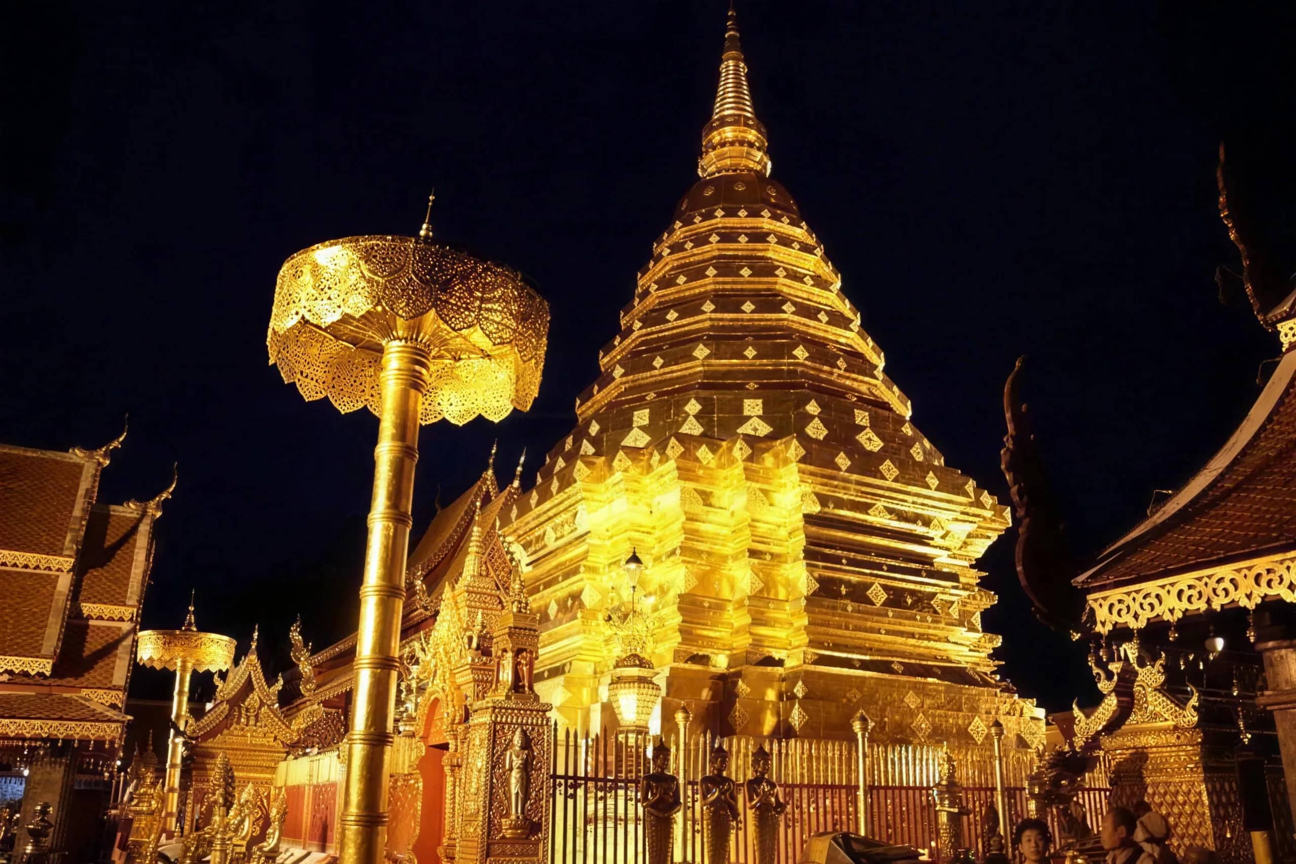 The illuminated golden chedi and parasol of Wat Phra That Doi Suthep against the night sky