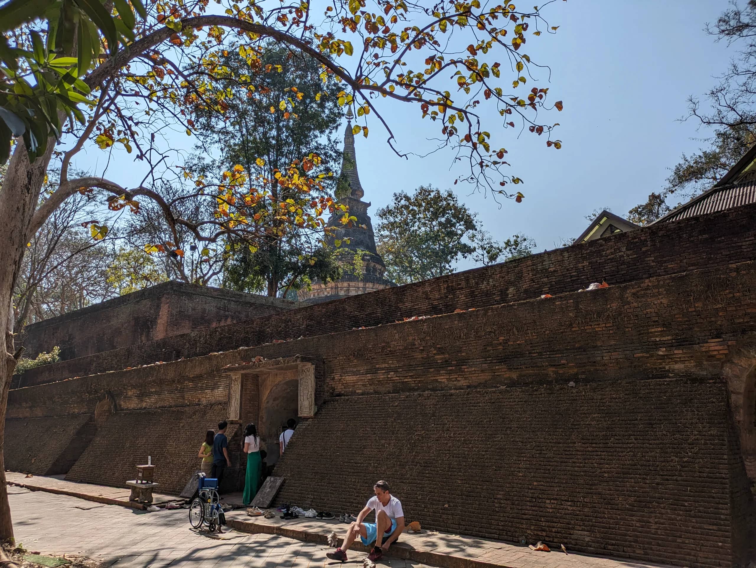 Visitors rest outside the old brick tunnel entrances of Wat Umong with a chedi rising behind