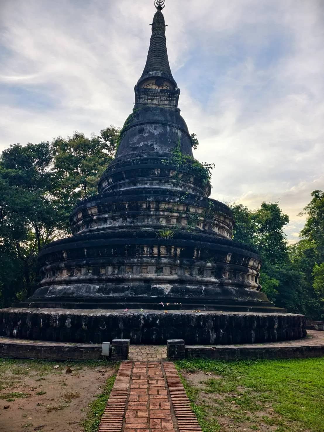 The dark weathered stone chedi of Wat Umong rises above a brick path and green lawn